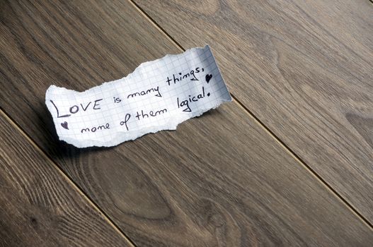 Love is many things, none of them logical (Quote by William Goldman) - Hand writing text on a piece of paper on wood background with space for text