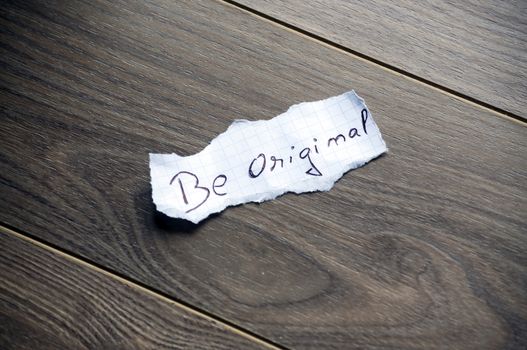 Be original written on piece of paper, on a wood background.