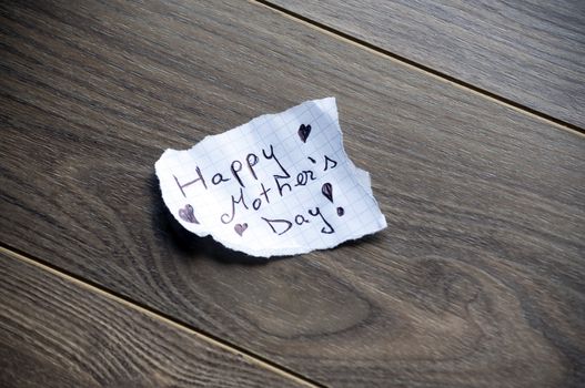 Happy Mother's Day written on piece of paper, on a wood background.
