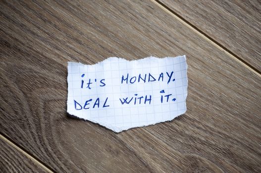 It's Monday. Deal With it written on piece of paper, on a wood background.