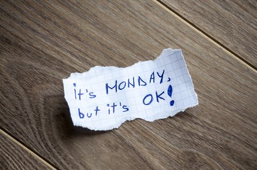 It's monday, but it's OK written on piece of paper, on a wood background.