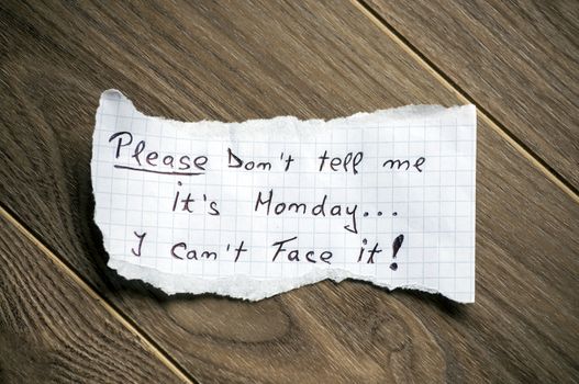 Monday message written on piece of paper, on a wood background.