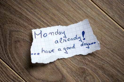 Monday already written on piece of paper, on a wood background.