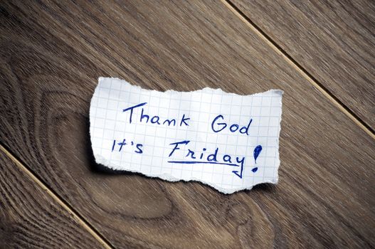 Friday message written on piece of paper, on a wood background.