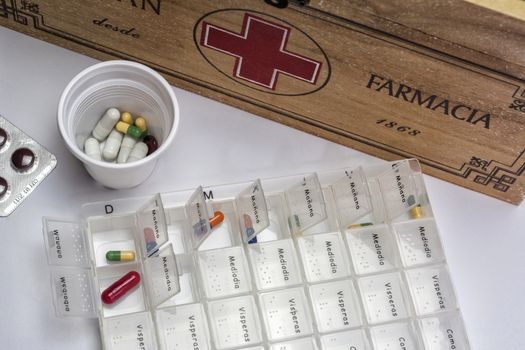 Pills with pill organizer next to old wood kit