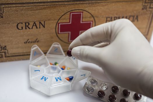 Hand with glove of white latex supports several tablets for classification, Pills with pill organizer next to old wood kit