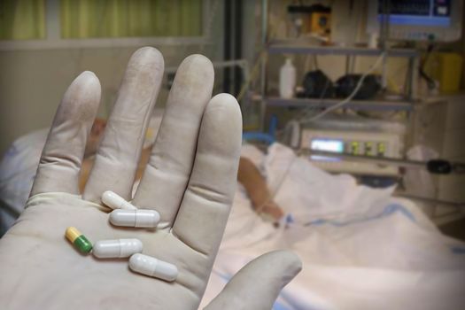 Hand with glove of white latex supports several tablets for classification, Pills with pill organizer next to old wood kit