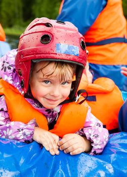 Happy little girl wearing helmet sitting in a rafting boat