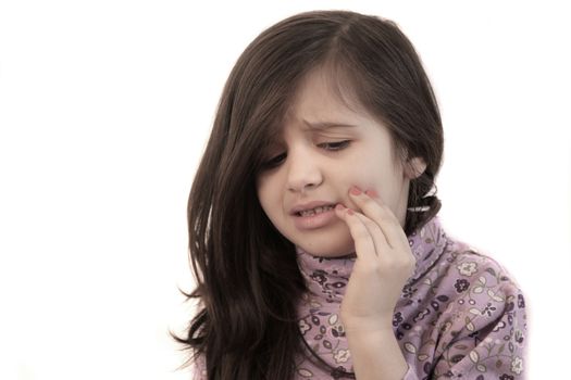 Cute little girl with her hand held to her face with painful expression showing toothache