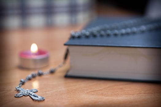 Rosary beads and a holy bible lighting by a red candle