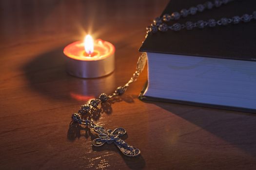 Rosary beads and a holy bible lighting by a red candle