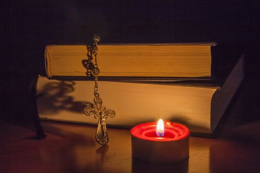 Rosary beads and a holy bible lighting by a red candle