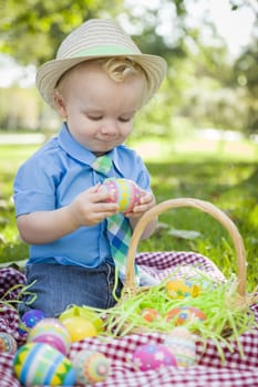 Cute Little Boy Wearing Hat Enjoying His Easter Eggs on Picnic Blanket Outside in the Park.