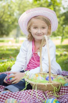 Cute Young Girl on Picnic Blanket Wearing Hat Enjoys Her Easter Eggs Outside in the Park.