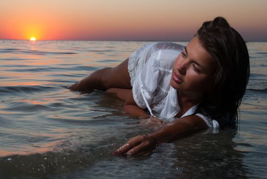 The attractive girl in a white wet transparent dress laying  in sea