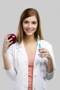 Beautiful and attractive female dentist holding tools and a red apple, isolated over a white background