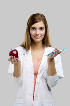 Beautiful and attractive female dentist holding tools and a red apple, isolated over a white background