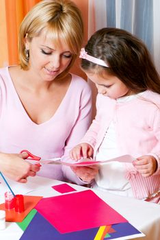 Mother and the daughter cut out figures from a colour paper