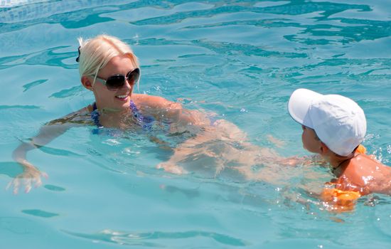 Smiling beautiful woman and little boy bathes in pool 