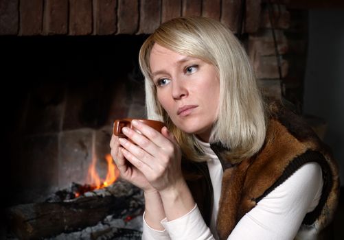 Portrait of beautiful woman with a mug near a fireplace