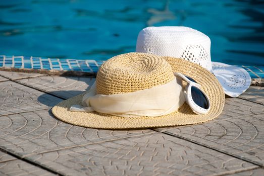 Straw hats and Sunglasses lies on the brink of pool 