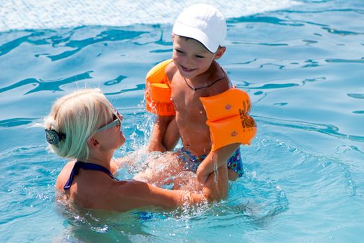 Smiling beautiful woman and little boy bathes in pool 