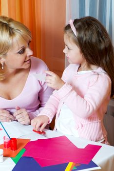 Mother and the daughter cut out figures from a colour paper