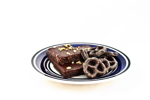 Chocolate covered pretzels and walnut-covered fudge brownie squares on a white and blue plate.