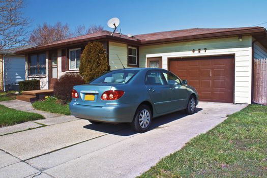 Modest one story home with compact car in the driveway. 