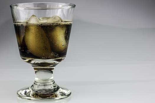 Amber liquid and ice cubes fill this small glass goblet.