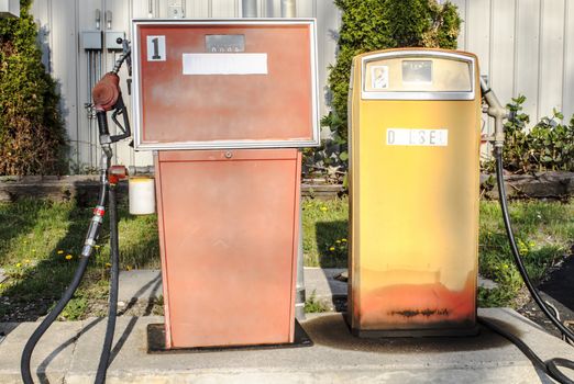 Two antique fueling machines. The paint is dulled and the lettering is wearing off. 