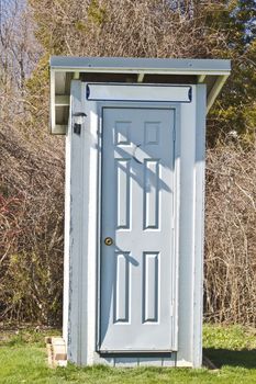 Newly constructed outhouse with gray door and white paneling. 