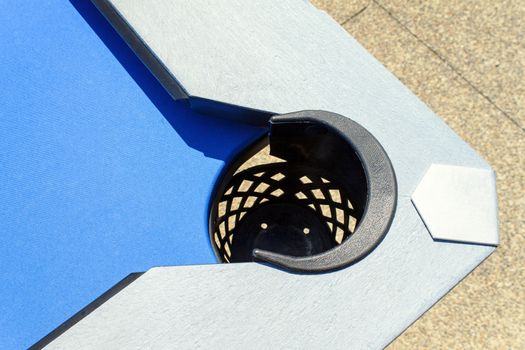 Black netted corner pocket of an outdoor pool table. 