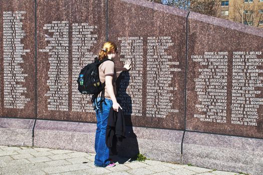 Woman stands thoughtfully with hand on memorial wall. 