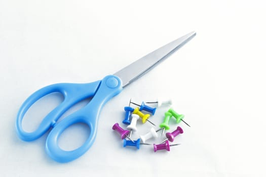 Blue handle scissors lay next to a pile of colorful tacks.