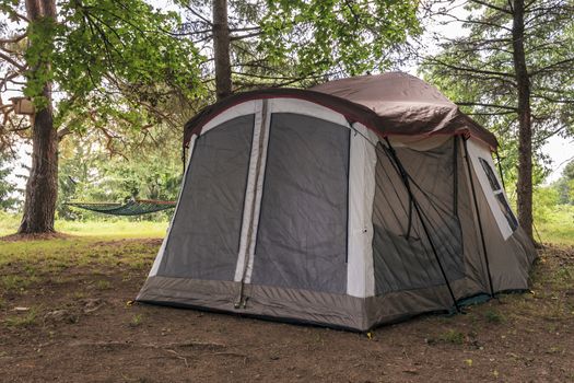 Tan and modern family tent set up under the pines. Zippered door and metal poles.