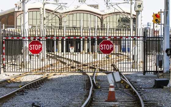 Closed gate to the train station. Stop lights, signs, and caution tape decorate the iron fence. 