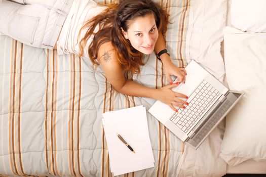 A young adult girl studying on the bed with a Laptop.