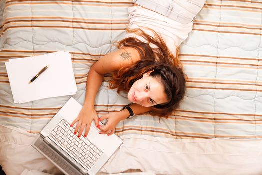 A young adult girl studying on the bed with a Laptop.