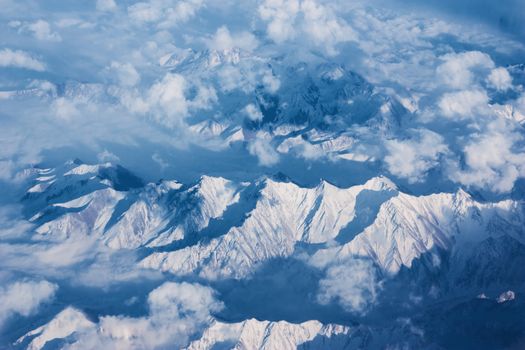 Top view of mountains with snow and clouds.