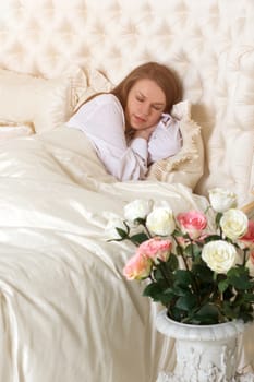 Romance. Beautiful sleeping woman in white bed with red roses