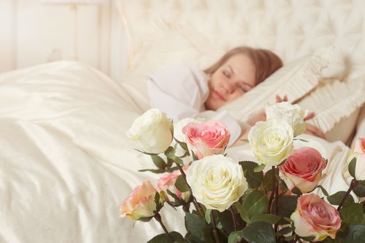 Romance. Beautiful sleeping woman in white bed with red roses