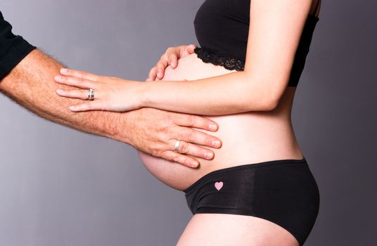 Pregnant woman standing touches belly with man