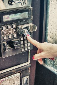 Woman finger pressing public telephone keyboard.