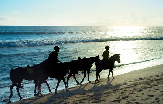 People riding a horses on the beach of Bali at sunset , Indonesia