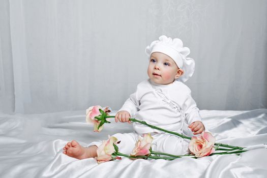 Little girl sitting on silk sheets lie at the feet of flowers