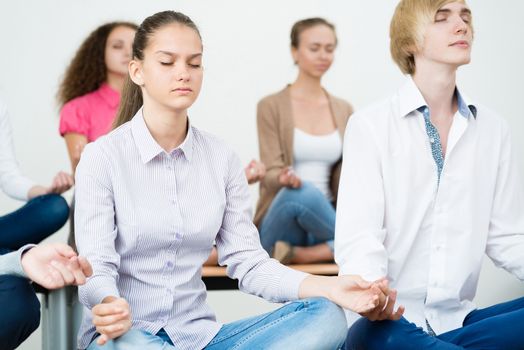 group of young people meditating in office at desk, group meditation