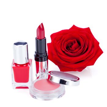 Display of fashionable cosmetics in their containers including a compact of powder or blusher, nail varnish and lipstick with a natural fresh red rose