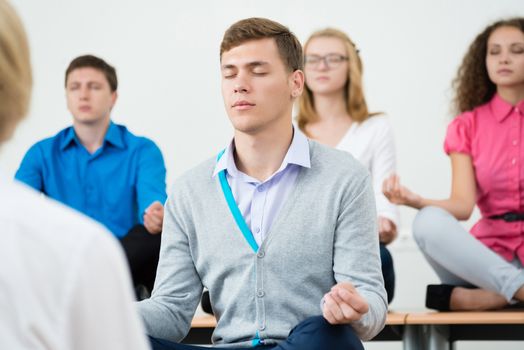 group of young people meditating in office at desk, group meditation