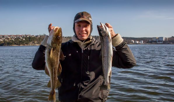 a boy holding a cod and a trout in his hands